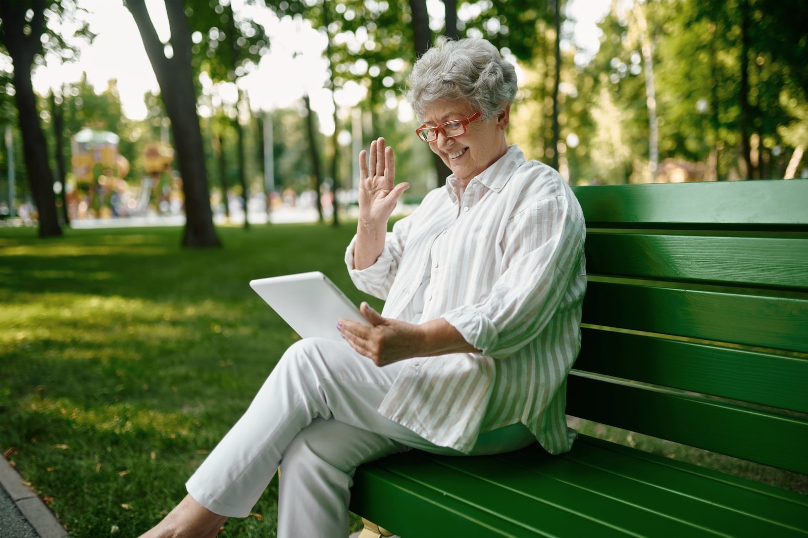 An elderly woman in glasses using laptop on bench